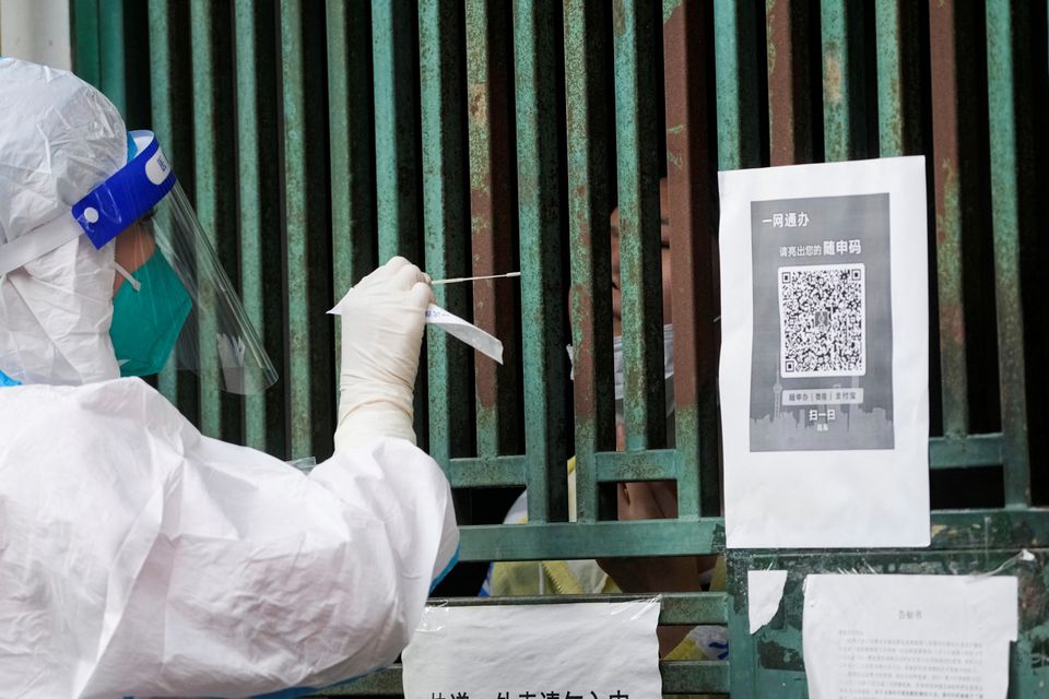 A medical worker in a protective suit collects a swab sample from a resident for nucleic acid testing, outside a closed entrance of a building during lockdown. (Reuters) A medical worker in a protective suit collects a swab sample from a resident for nucleic acid testing, outside a closed entrance of a building during lockdown. (Reuters)