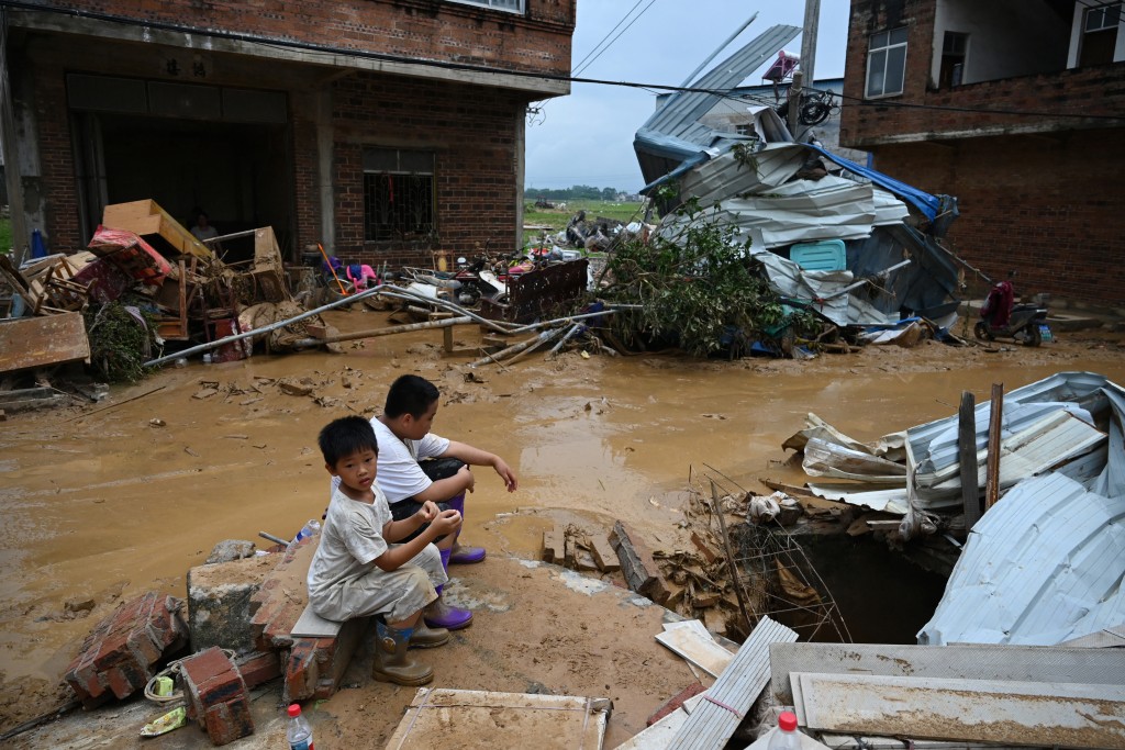 Photo by GREG BAKER / AFP Children sit next to houses which were damaged when the Liulan reservoir collapsed on July 6, in Liulan village, in Hengzhou city, in China’s southwest Guangxi region on July 8, 2026.
