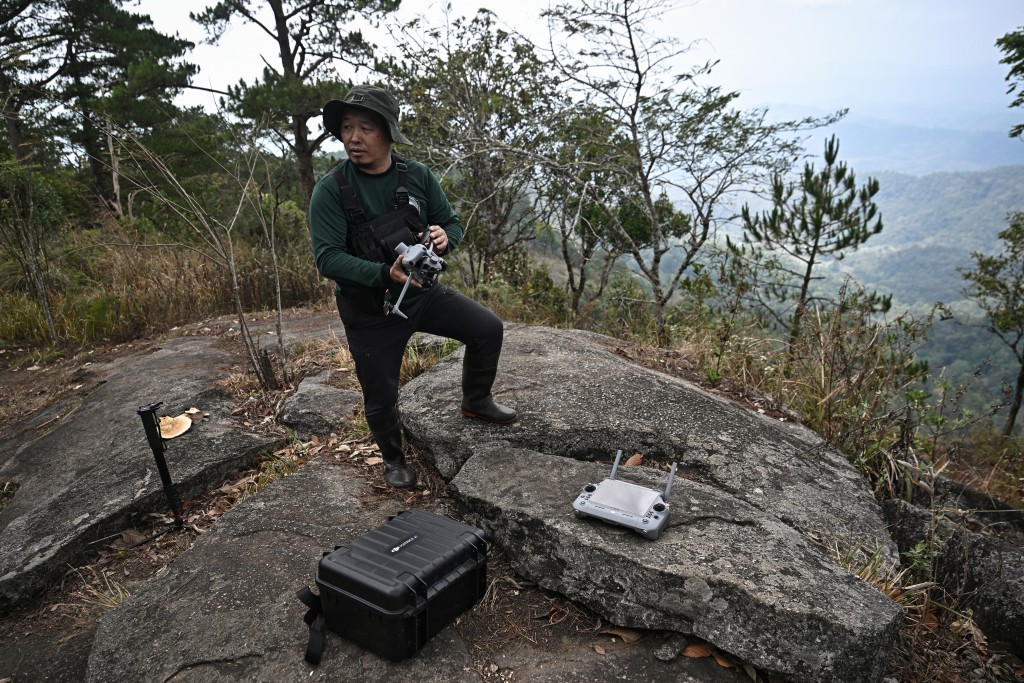 Photo by LILLIAN SUWANRUMPHA / AFP  This photo taken on March 16, 2026 shows Hmong volunteer firefighter Mongkol Yingyotmongkolsaen using a drone to monitor fires in the Doi Suthep-Pui National Park area of Chiang Mai.