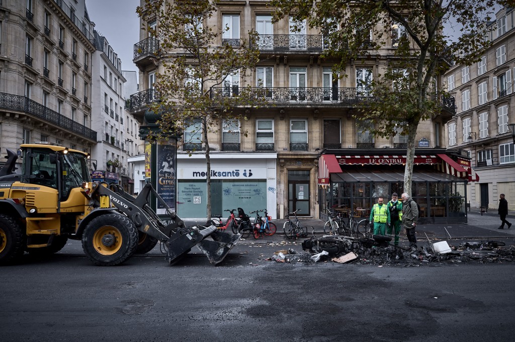 Municipal workers and a member of the public look at the burnt out remains of a barricade on Boulevard de Sebastapol during a clean up of the capital after a weekend of protests against the "high cost of living", in central Paris on October 19, 2026.