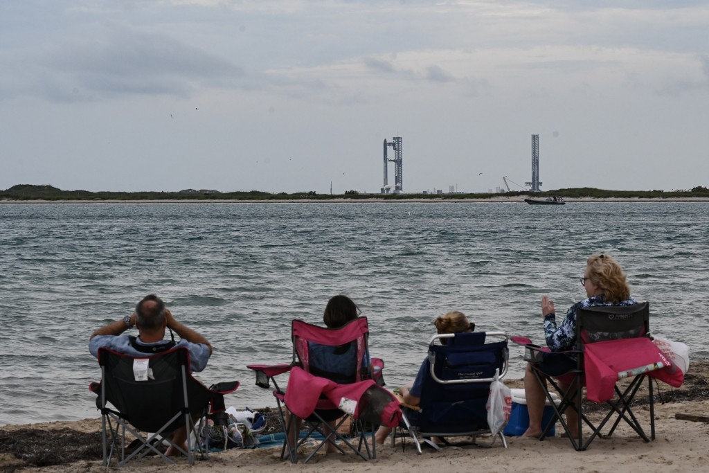 People look at the SpaceX Starship rocket in Starbase, Texas, as seen from South Padre Island on August 25, 2025. Elon Musk's SpaceX postponed the latest test launch of its massive prototype Starship rocket on August 25, 2025 because of bad weather, the company said on a live webcast. (Photo by RONALDO SCHEMIDT / AFP)
