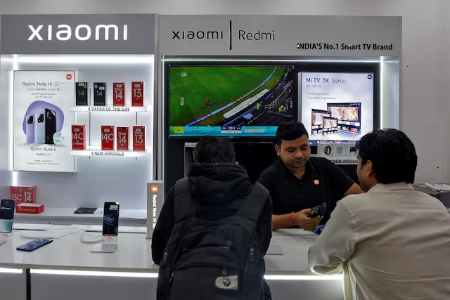 A salesperson shows a new Xiaomi mobile phone to customers at a store in New Delhi, India, February 1, 2025. REUTERS/Priyanshu Singh