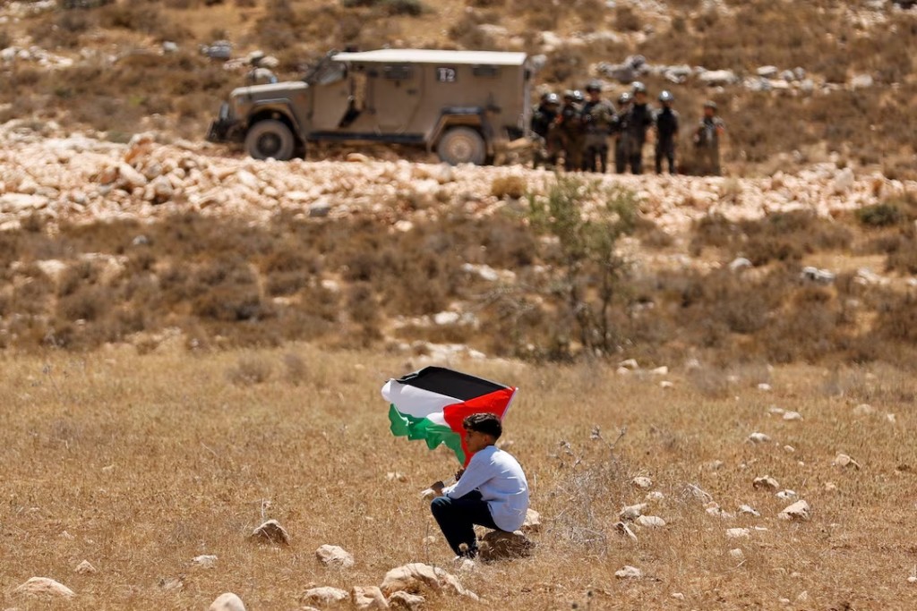A boy holds a Palestinian flag during a demonstration against what Palestinians say is Israel's confiscation of their land, as Isareli security forces stand guard, in Raba, near Jenin, in the Israeli-occupied West Bank July 18, 2025. REUTERS/Raneen Sawafta TPX IMAGES OF THE DAY