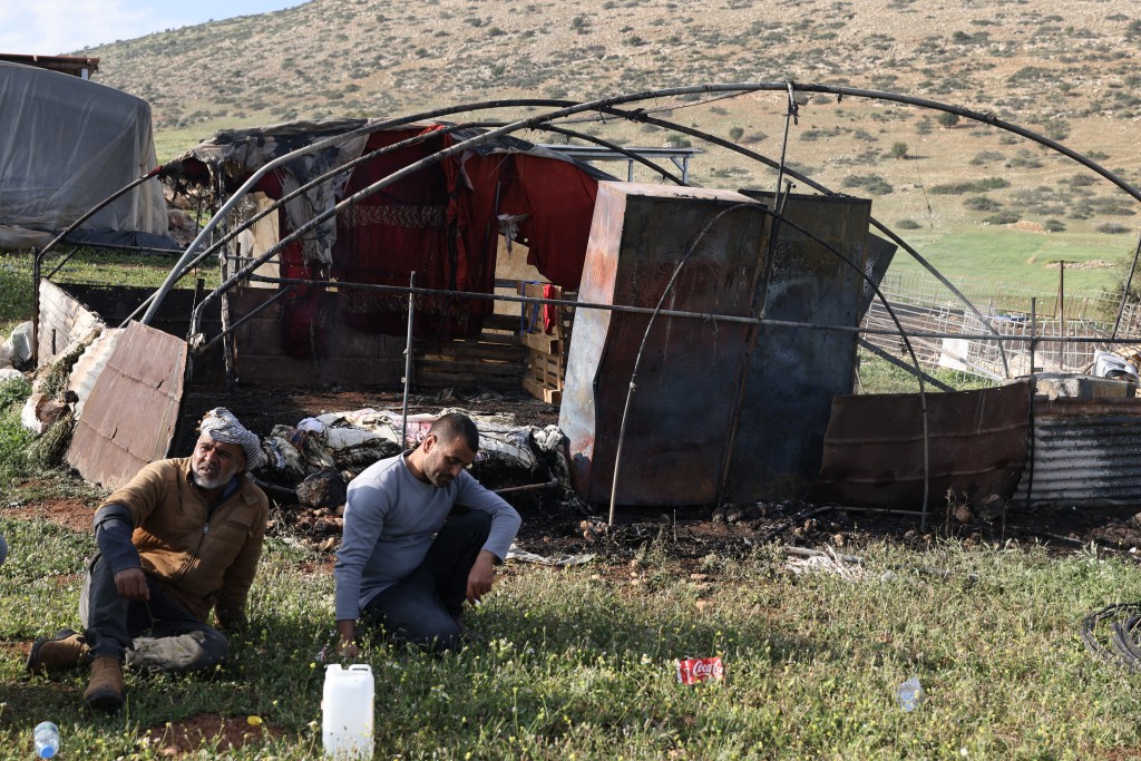 Photo by JAAFAR ASHTIYEH / AFP. Palestinian men sit next to their burned property following an Israeli settlers attack in the northen outskirts of Tayasir village near the occupied West Bank town of Tubas on March 31, 2026.