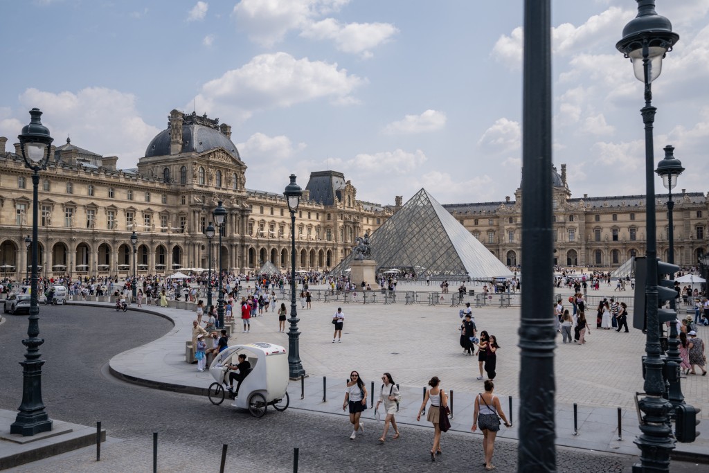 Tourists walk past the Louvre Museum and the Pyramide du Louvre, designed by Chinese-US architect Ieoh Ming Pei, in central Paris on July 18, 2026. (Photo by Martin LELIEVRE / AFP)