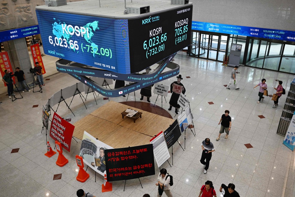 People walk below a stock index board showing South Korea's benchmark stock index (KOSPI) after the close of trading in Seoul on July 28, 2026. AFP