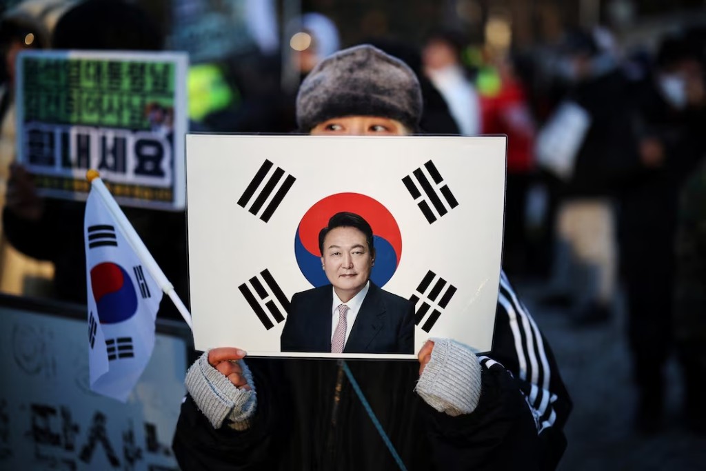  A woman holds a sign bearing South Korean national flag with a portrait of former President Yoon Suk Yeol, as they wait for his arrival for the final arguments in his insurrection trial, at a court in Seoul, South Korea, January 13, 2026. REUTERS/Kim Hong-Ji 