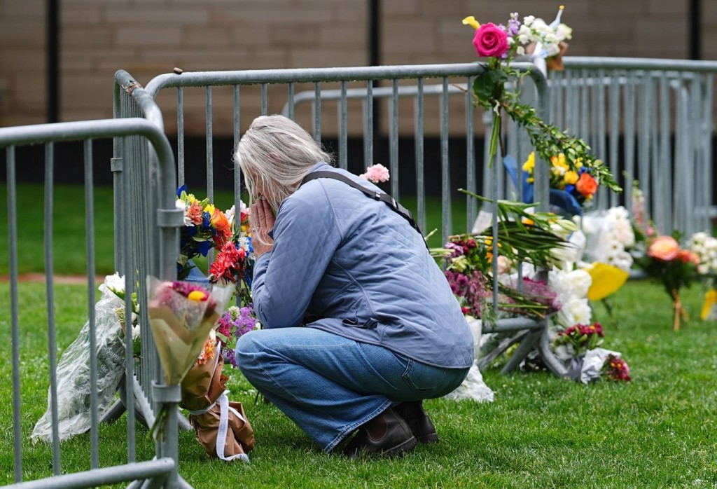 A visitor offers a tribute after leaving a bouquet of flowers at a makeshift memorial for victims of an attack outside of the Boulder County, Colo., courthouse as a light rain falls Tuesday, June 3, 2025, in Boulder, Colo. (AP Photo/David Zalubowski)