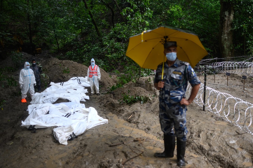 Photo by MANAN VATSYAYANA / AFP  Security personnel stand next to unidentified bodies of flood victims kept for mass burial at the Gokarna forest reserve in Kathmandu on September 1, 2026.