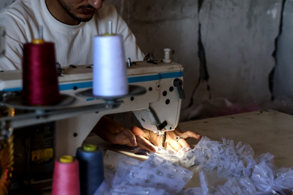 Photo by BASHAR TALEB / AFP A Palestinian dressmaker sits at a sewing machine as he assembles a gown, at a workshop where dresses are created including evening and wedding gowns despite limited resources and old dresses are recycled, in the city of Khan Yunis in the southern Gaza Strip on June 13, 2026.