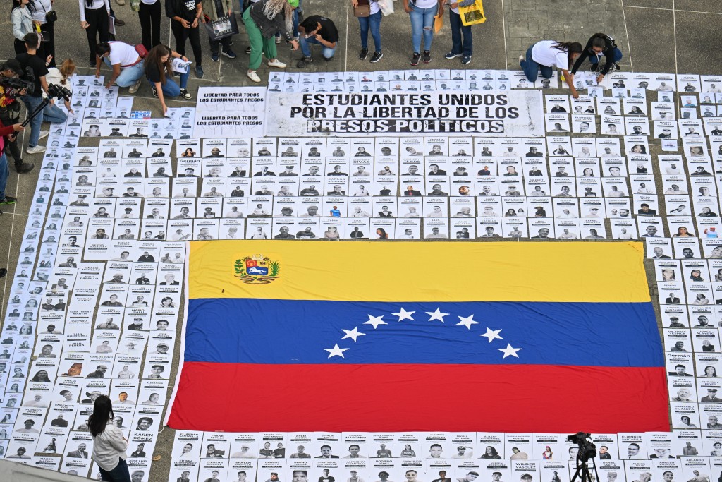 Photo by JUAN BARRETO / AFP  People display portraits of political prisoners during a demonstration by relatives at the Central University of Venezuela in Caracas on January 13, 2026.