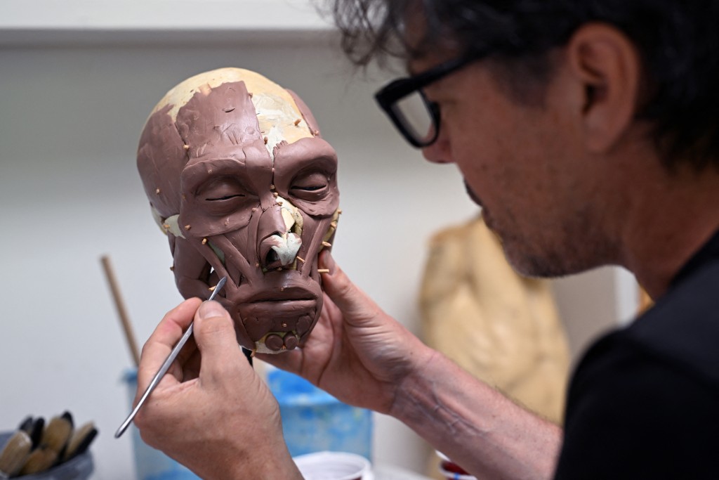 Dutch artist Alfons Kennis works on a model representing a prehistoric human skull in his workshop in Arnhem, on July 3, 2025. Alfons and his twin brother Adrie are known for their paleo-anthropological work. Using a combination of forensic modelling and genetic insights, they craft an intimate representation of this ancient individuals, including recently a mesolithic individual known as the "Margaux woman". (Photo by Nicolas TUCAT / AFP)