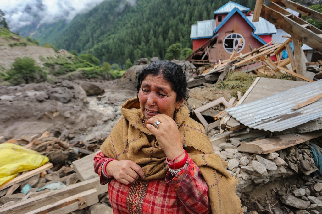 A woman breaks down as she stands near a damaged house at the site of a flashflood at a village in Kishtwar district on August 15, 2025. Indian rescuers pulled bodies from mud and rubble August 15 after the latest deadly flood to crash through a Himalayan village killed at least 60 people and washed away dozens more. (Photo by Mir Imran / AFP)