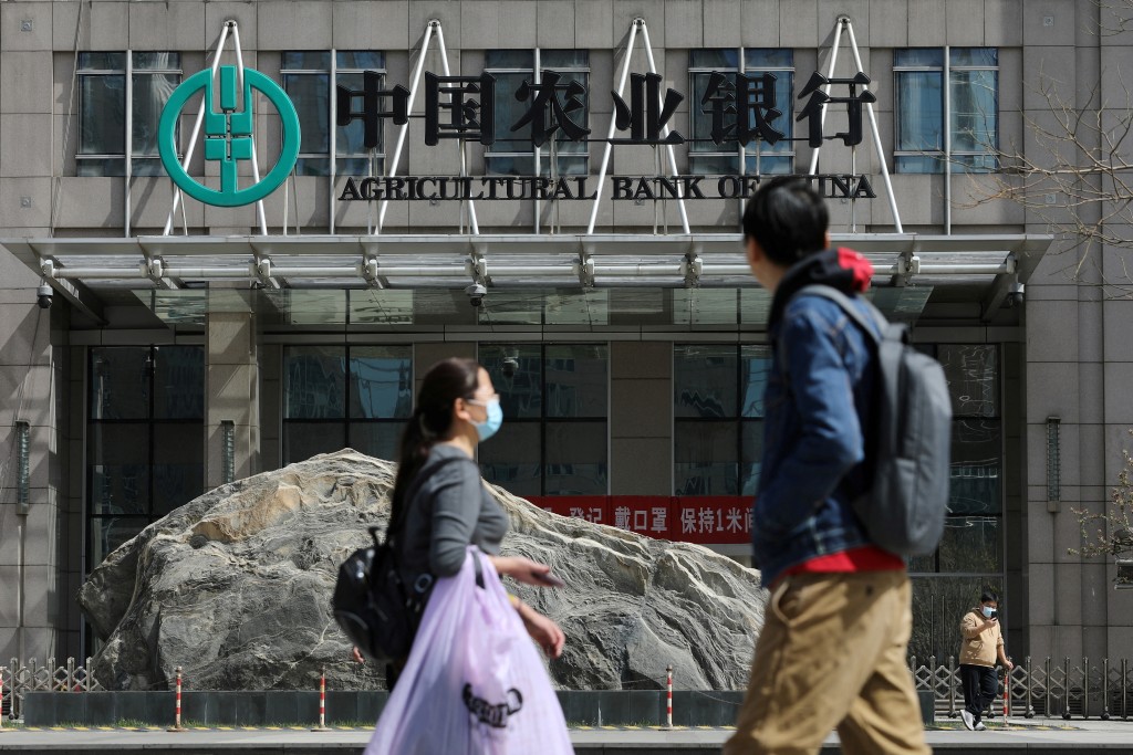 People walk past an office building of Agricultural Bank of China, in Beijing, China March 29, 2021. REUTERS