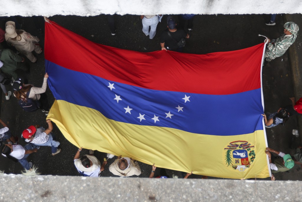 Photo by PEDRO MATTEY / AFP. People hold a Venezuelan flag during a demonstration in support of deposed Venezuelan President Nicolas Maduro and his wife, Cilia Flores, in Caracas on January 16, 2026.