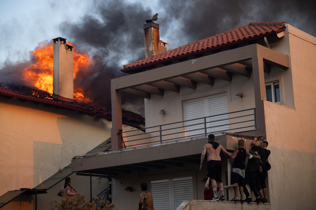 Local residents try to extinguish the fire of a burning house during a wildfire in Kryoneri, near Athens on July 26, 2025. (AFP)