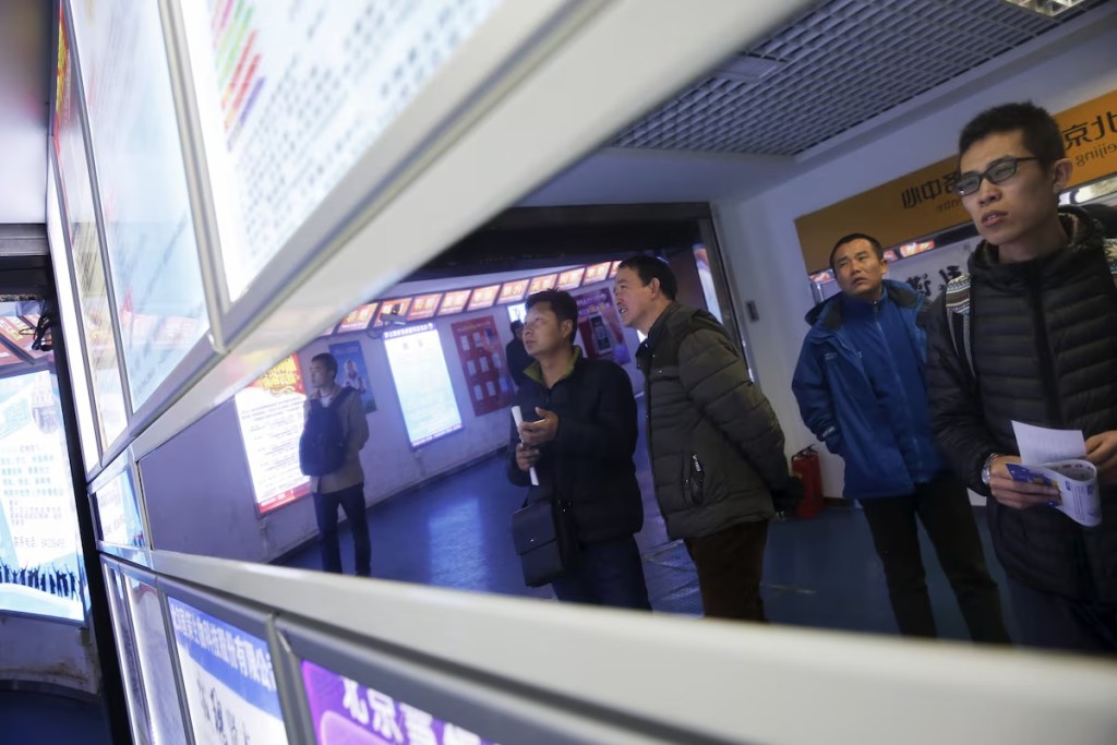 People are reflected in mirror as they read notices displayed at a job fair in Beijing, China February 24, 2016. REUTERS