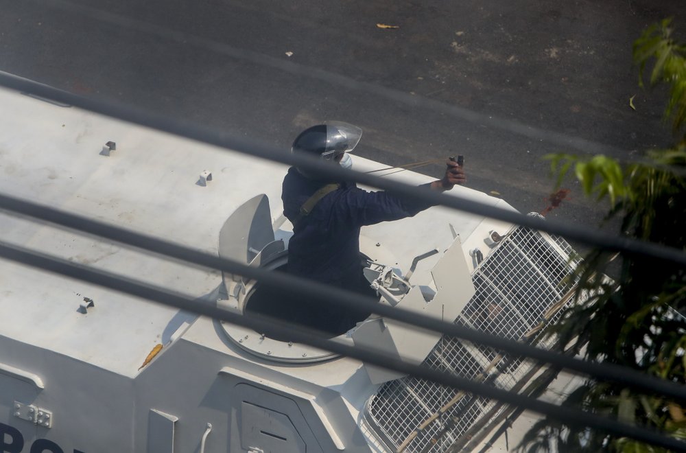 A policeman popping out from a police vehicle aims a slingshot towards anti-coup protesters in Mandalay, Myanmar, Wednesday, March 3, 2021.
