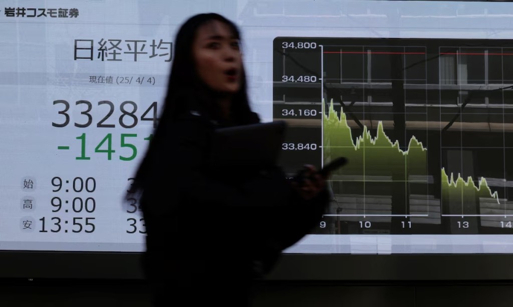 A pedestrian walks past a stock quotation board showing Nikkei share average outside a brokerage in Tokyo, Japan April 4, 2025. REUTERS