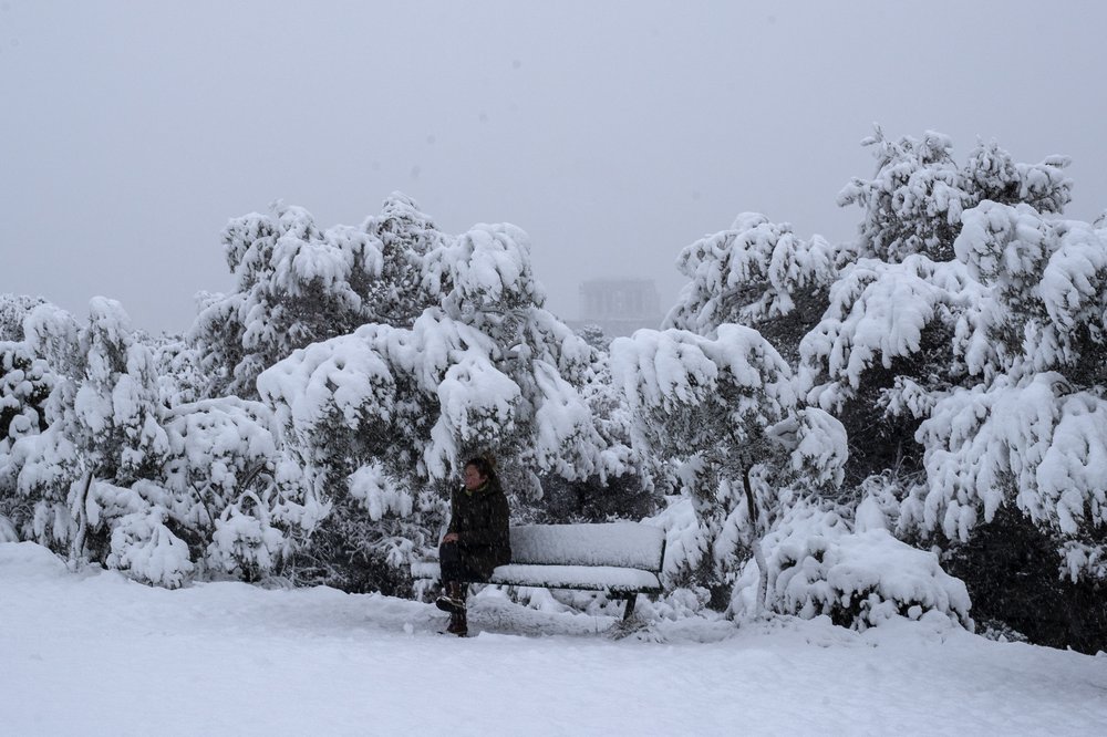 A woman sits on a snow-covered bench in front of the Parthenon temple, in Athens, Tuesday.