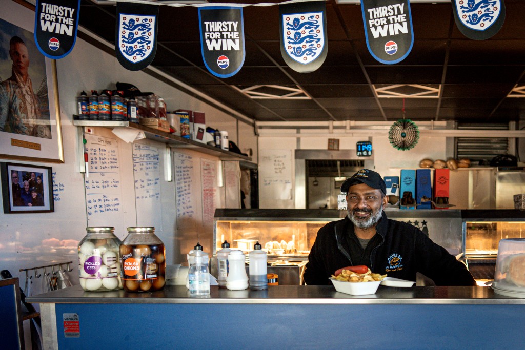Photo by MARK NAFTALIN / AFP  Sailish Parekh stands behind the counter of his fish-and-chip shop near the Etihad Stadium, in Manchester, central England on October 8, 2026.