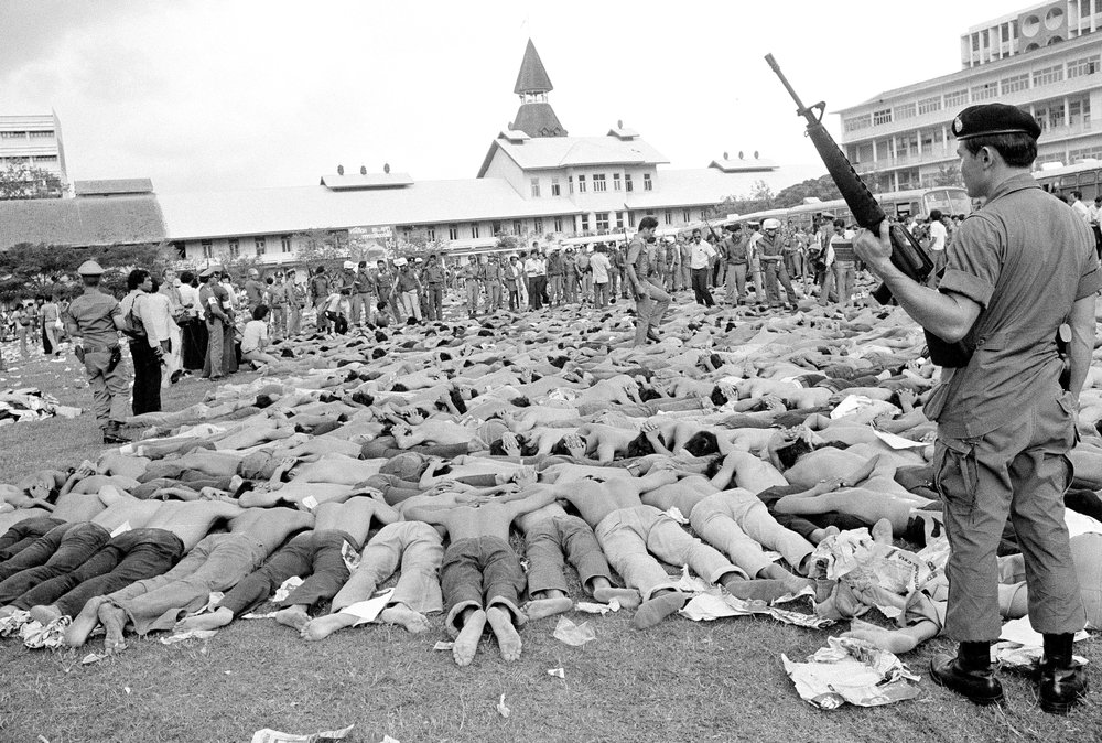 In this October 6, 1976, file photo, police stand guard over leftist Thai students on a soccer field at Thammasat University, in Bangkok, Thailand. In this October 6, 1976, file photo, police stand guard over leftist Thai students on a soccer field at Thammasat University, in Bangkok, Thailand.