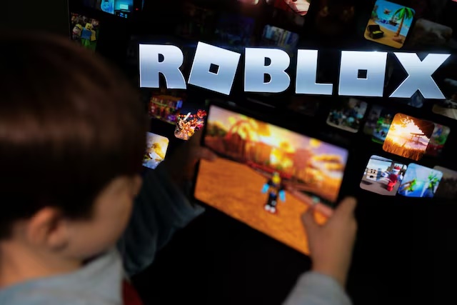 A boy poses for a photo while holding a game pad in front of a screen displaying the logo of the U.S. children's gaming platform Roblox, in this illustration taken December 8, 2025. REUTERS/Ramil Sitdikov/Illustration 