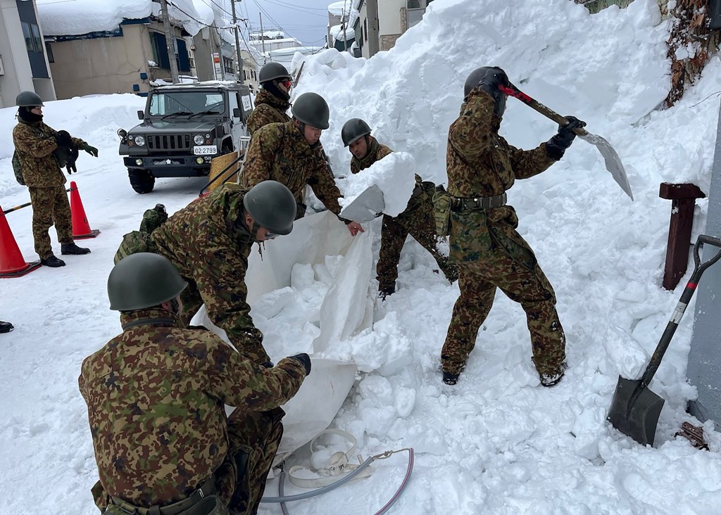 Photo by HANDOUT / JAPAN'S MINISTRY OF DEFENSE / AFP  This handout photo taken on February 3, 2026 and received on February 4, 2026 from Japan's Ministry of Defence shows members of the Japan Ground Self-Defence Force's 5th Infantry Regiment, stationed in Aomori Prefecture, carrying out snow removal work in a town within Aomori Prefecture.