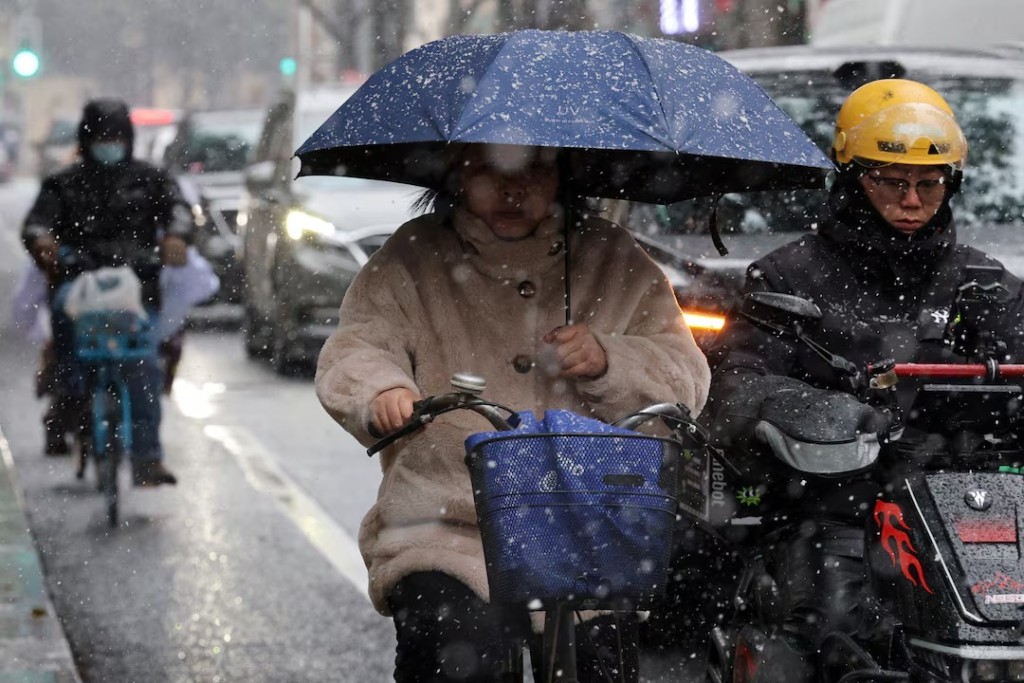 A woman holding an umbrella rides a bicycle amid snowfall in Shanghai, China January 20, 2026. REUTERS/Go Nakamura