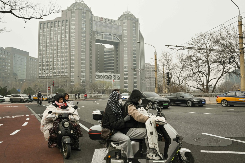 Motorists ride their vehicles past the Bank of China building in Beijing on March 11, 2025. (Photo by ADEK BERRY / AFP)