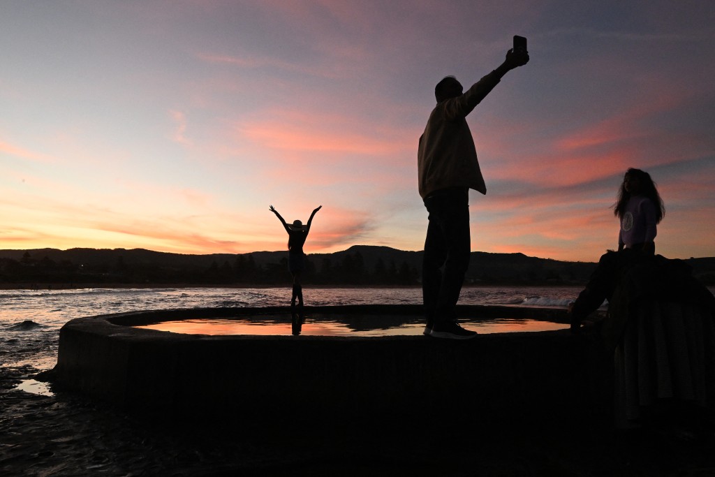 Photo by SAEED KHAN / AFP  This picture taken on April 27, 2026 shows tourists photographing the sunset at the end of a well-known street in Gerringong, around a two-hour drive south of Sydney.