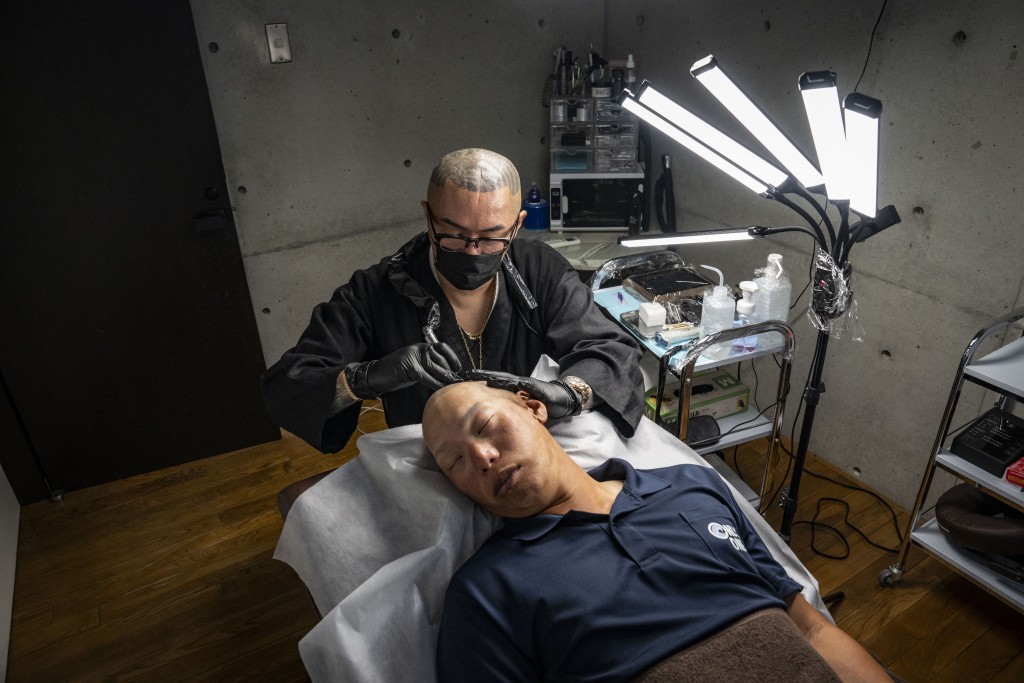 Photo by YUICHI YAMAZAKI / AFP  This picture taken on May 19, 2026 shows scalp tattoo artist Remy (top) performing scalp micropigmentation procedure on client Koki Hatanaka at his studio in Ginowan, Okinawa prefecture.