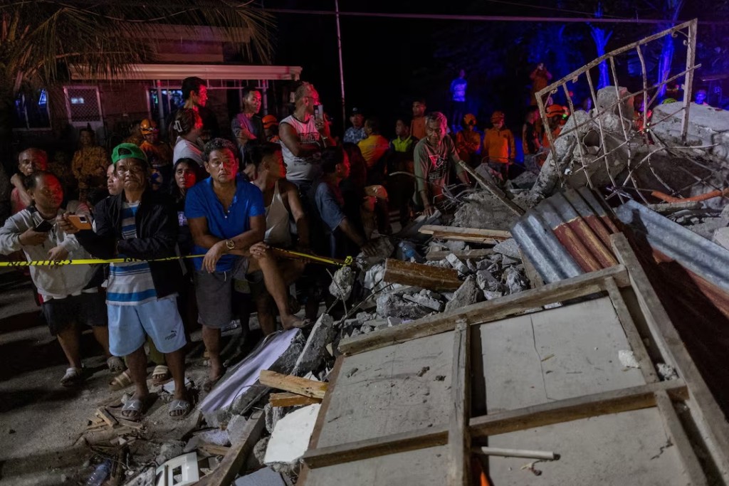 Residents watch as rescuers retrieve bodies of victims found under the rubble of a damaged pension house in the aftermath of a magnitude 6.9 quake in Bogo, Cebu, Philippines, October 1, 2025. REUTERS/Eloisa Lopez 