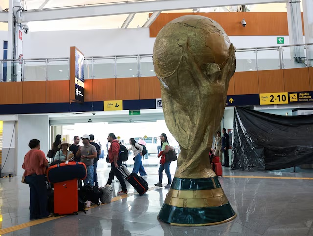Passengers stand beside a giant replica of the World Cup trophy displayed at Mexico City International Airport, ahead of the World Cup starting on June 11, in Mexico City, Mexico, May 15, 2026. REUTERS/Henry Romero