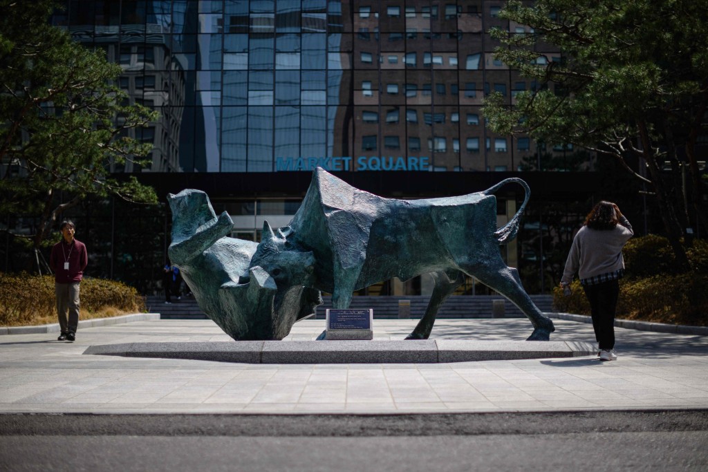People walk past a bull and bear sculpture in front of the Korea Exchange building in Seoul on April 7, 2025. Asian equities collapsed on a black Monday on April 7 for markets after China hammered the United States with its own hefty tariffs, ramping up a trade war many fear could spark a recession. (Photo by ANTHONY WALLACE / AFP)