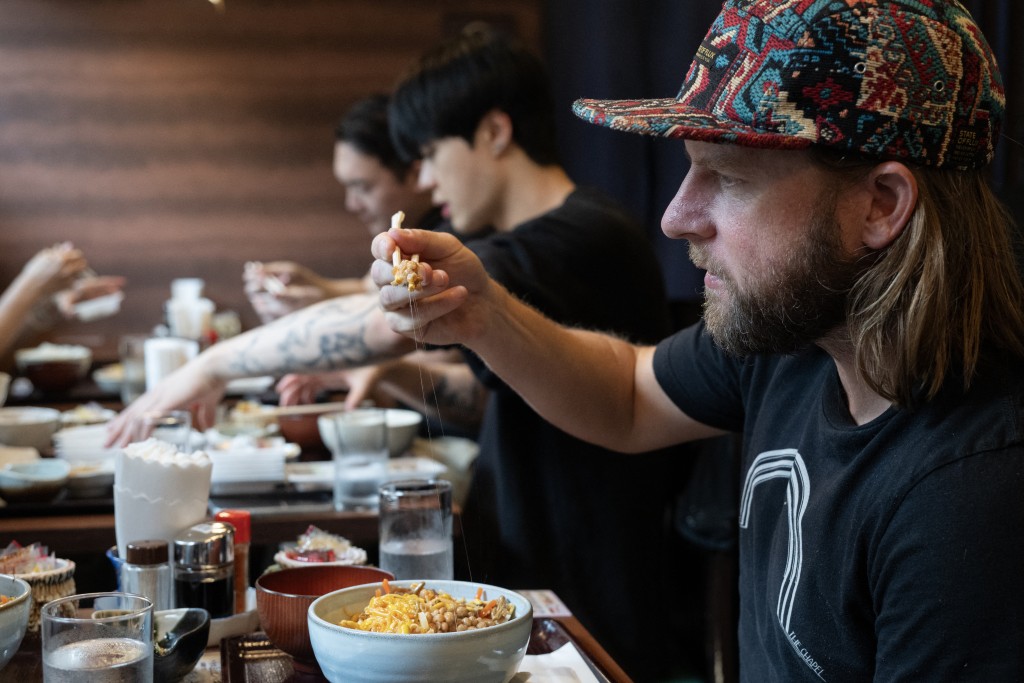 Photo by ANDREW CABALLERO-REYNOLDS / AFP This photo taken on June 8, 2026 shows US tourist Wesley Smith looking at natto on his chopsticks as he eats lunch at the Natto Kobo Sendai-ya restaurant in Tokyo.