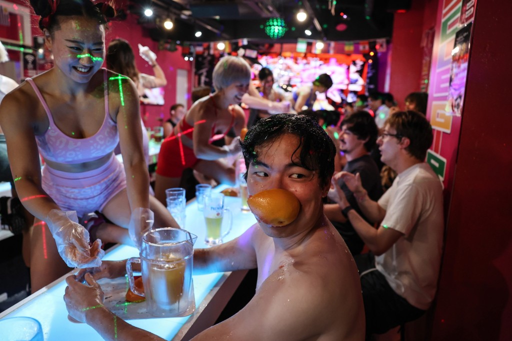 A male customer holds part of a grapefruit in his mouth after Muscle Girls staffer Risa Matsuda, 27, crushed the grapefruit with her bare hands while making a drink in Tokyo, Japan, July 25, 2025. REUTERS/Kim Kyung-Hoon