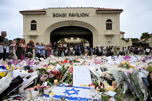 People stand near flowers laid as a tribute at Bondi Beach to honour the victims of a mass shooting that targeted a Hanukkah celebration at Bondi Beach on Sunday, in Sydney, Australia, December 16, 2025. REUTERS/Flavio Brancaleone/File Photo