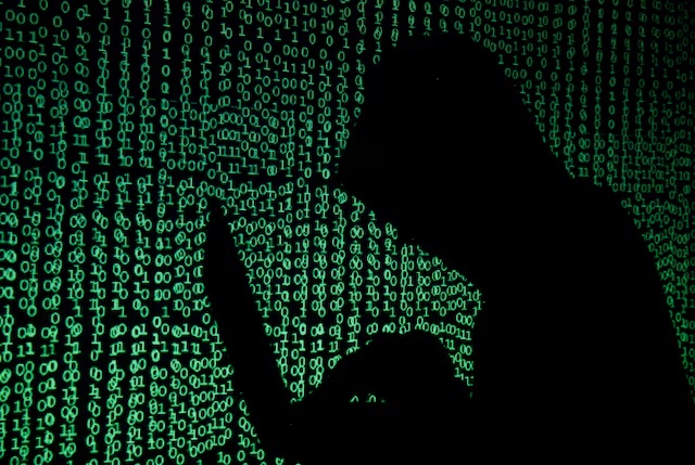 A hooded man holds a laptop computer as cyber code is projected on him in this illustration picture taken on May 13, 2017. REUTERS/Kacper Pempel/Illustration/File Photo