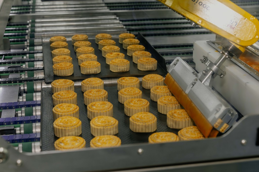 A robotic egg-wash arm applies egg wash to mooncakes with controlled pressure and angles for more even browning.