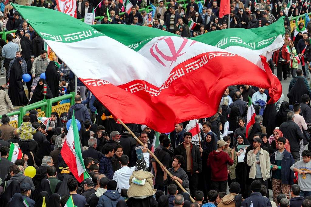 Photo by - / AFP  A man waves a giant Iranian flag during a rally marking the 47th anniversary of the 1979 Islamic revolution in Tehran on February 11, 2026.