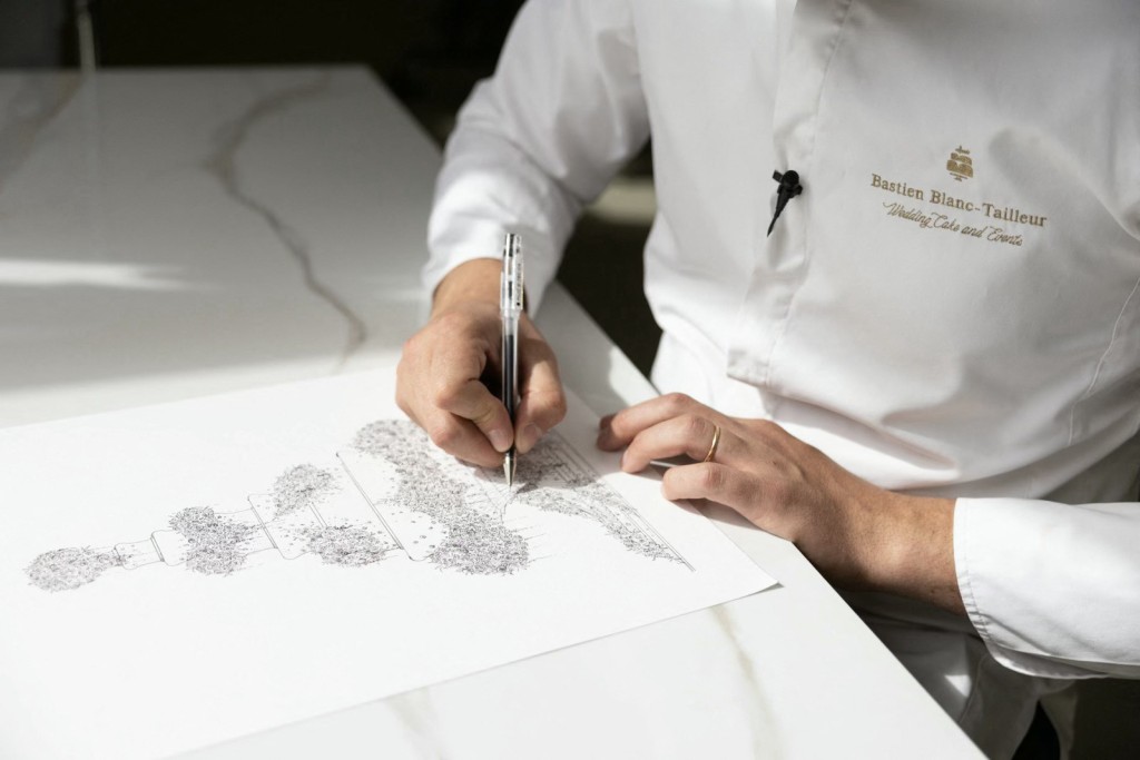 Photo by THOMAS SAMSON / AFP  French pastry chef Bastien Blanc-Tailleur designs a wedding cake at his studio in Saint-Remy-les-Chevreuse, southwestern Paris on April 10, 2026.