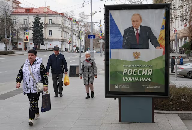 People walk past a banner depicting Russian President Vladimir Putin in Sevastopol, Crimea March 22, 2025. REUTERS/Alexey Pavlishak/File Photo