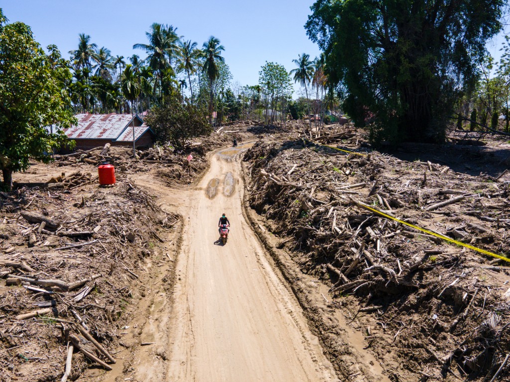 Photo by CHAIDEER MAHYUDDIN / AFP  An aerial view shows a person riding a motorcycle past flash flood damage at a residential area in Meurah Dua, Aceh province's Pidie Jaya district on February 22, 2026, after devastating floods and landslides struck Indonesia's Sumatra late last year.