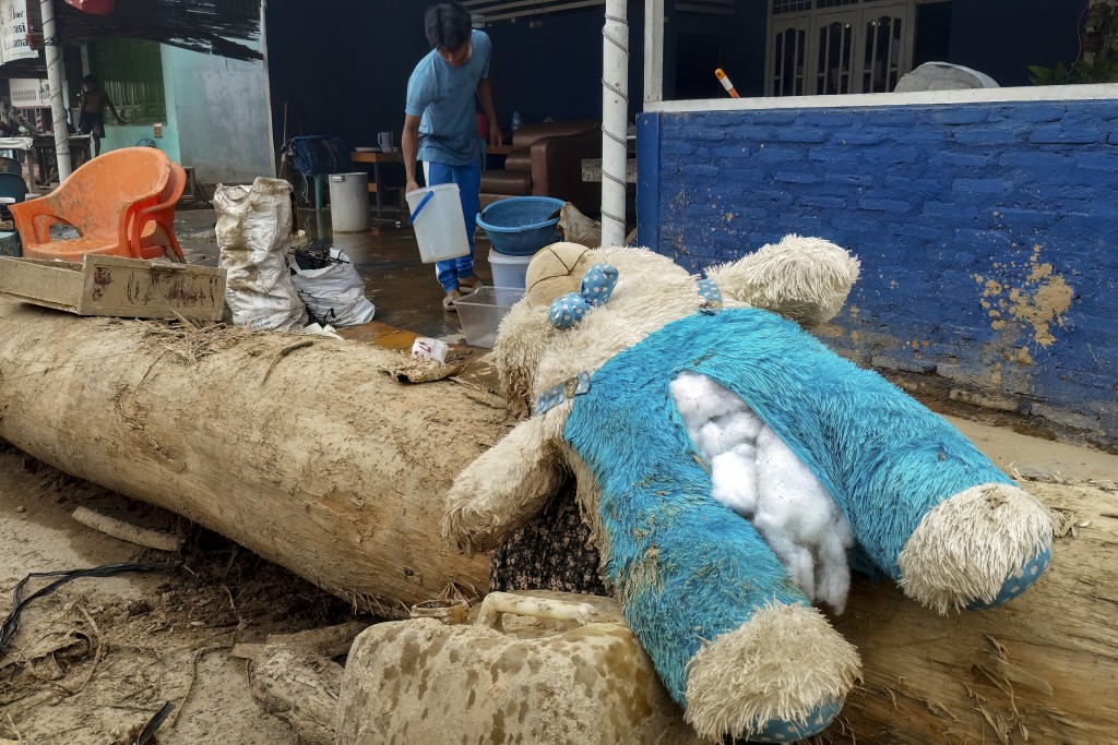 A damage bunny doll is being sun-dried next to a villager affected by flash floods clearing mud from his home in Central Tapanuli, North Sumatra province on December 5, 2025. (Photo by DAMAI MENDROFA / AFP)