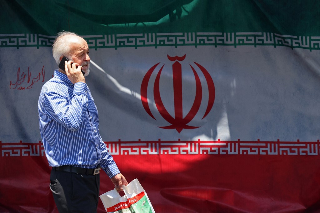 Photo by ATTA KENARE / AFP A man walks past Iran's national flag at the Vanak Square in Tehran on June 10, 2026.
