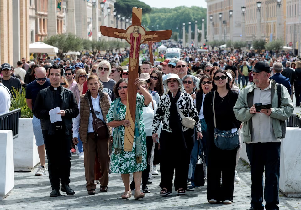 A woman carries a cross as people walk, after the death of Pope Francis was announced by the Vatican in a video statement, as seen from Rome, Italy, April 21, 2025. REUTERS/Remo Casilli