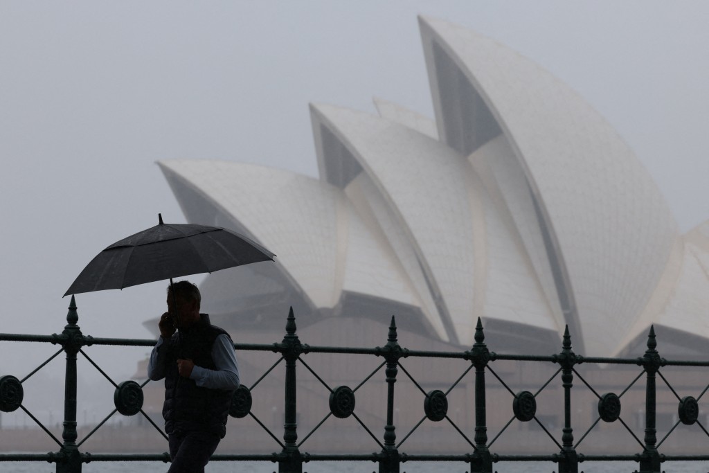A man carrying an umbrella walks past the Sydney Opera House in Sydney, Australia, November 21, 2025. (Reuters)