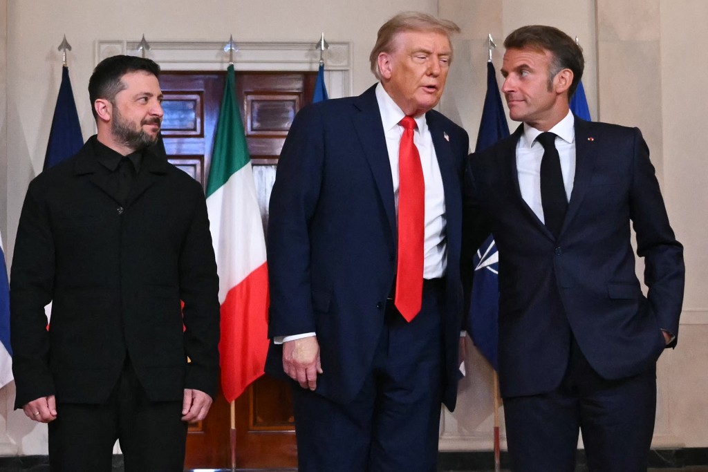 Ukrainian President Volodymyr Zelensky, US President Donald Trump, and French President Emmanuel Macron stand for a family photo with European leaders in the Cross Hall of the White House in Washington, DC, on August 18, 2025. European leaders join Ukrainian President Volodymyr Zelensky in talks with US President Donald Trump on August 18. (Photo by ANDREW CABALLERO-REYNOLDS / AFP)