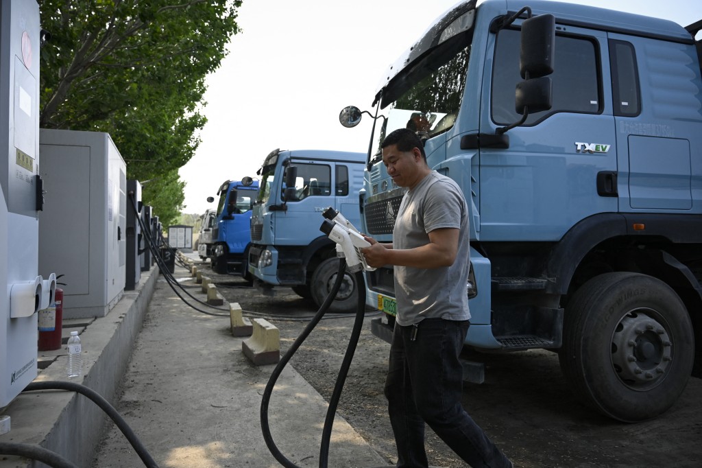 Photo by WANG ZHAO / AFP  This picture taken on April 23, 2026 shows a driver returning the charging gun after charging his electric truck at a station in Beijing.